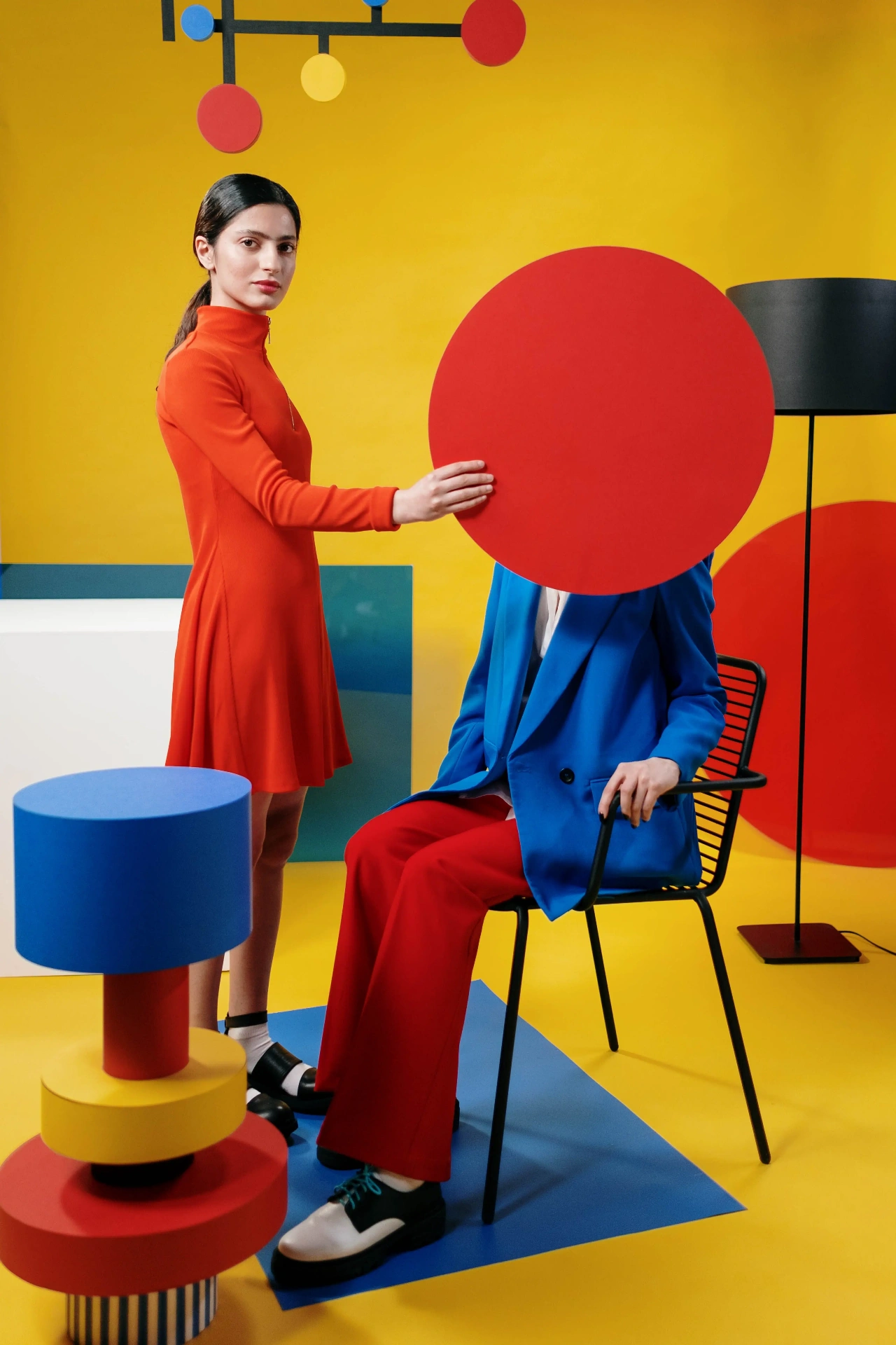 Two models in a De Stijl staged interior with mobile, chair, and lamp, by cottonbro studio.
