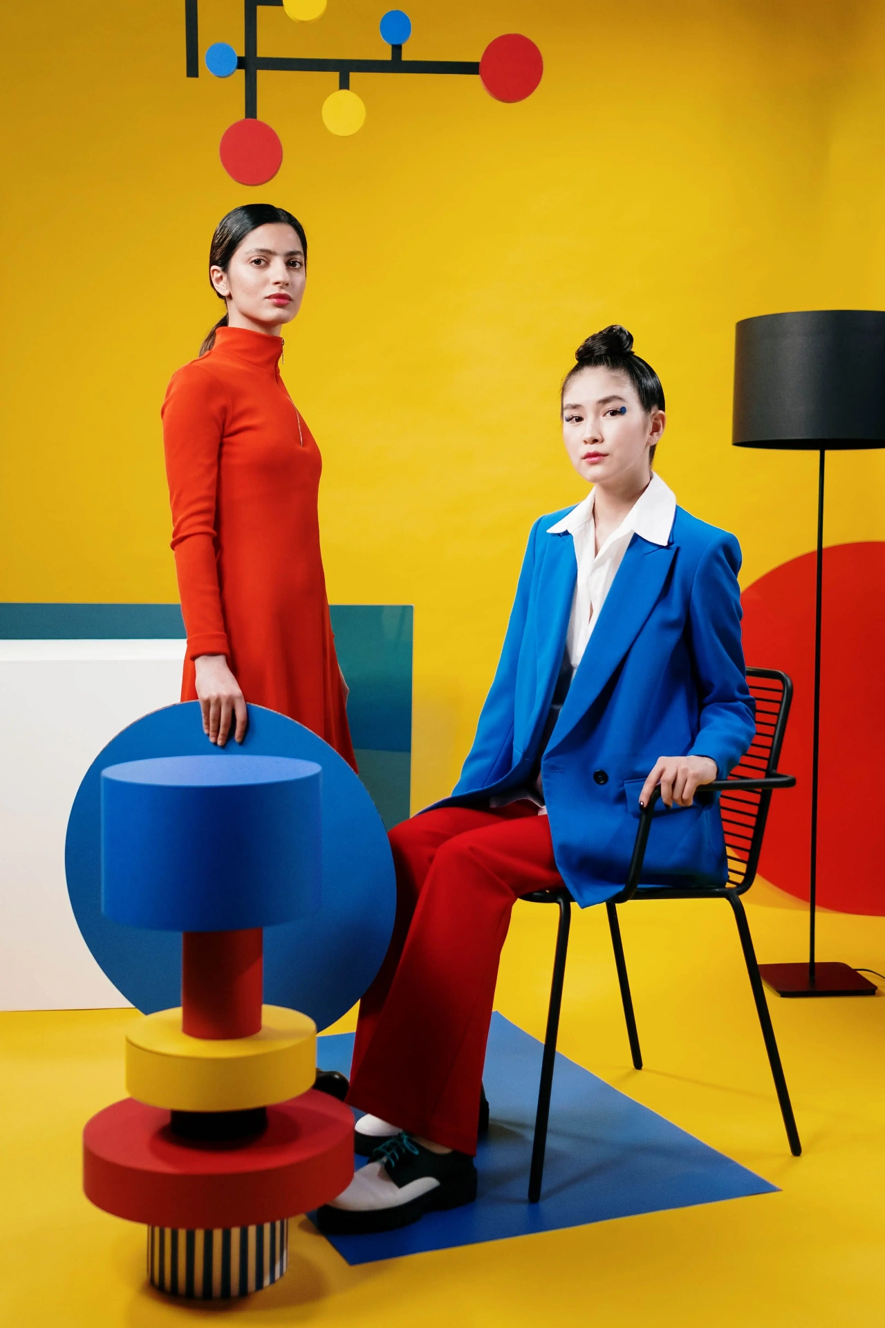 Two models — one in a red dress, one in a blue blazer — with vivid geometric props, by cottonbro studio.