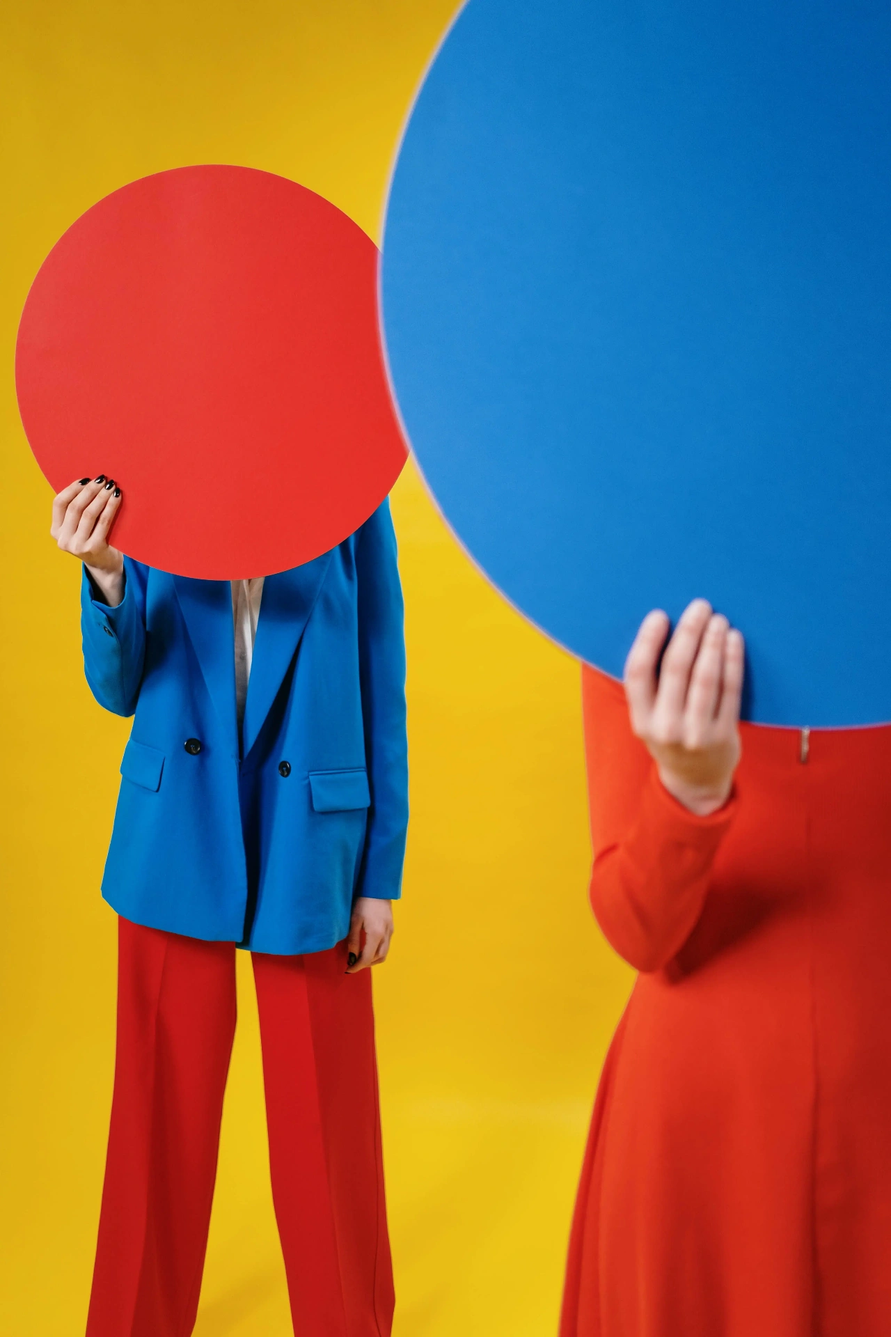 Two models holding large red and blue paper circles obscuring their faces, by cottonbro studio.