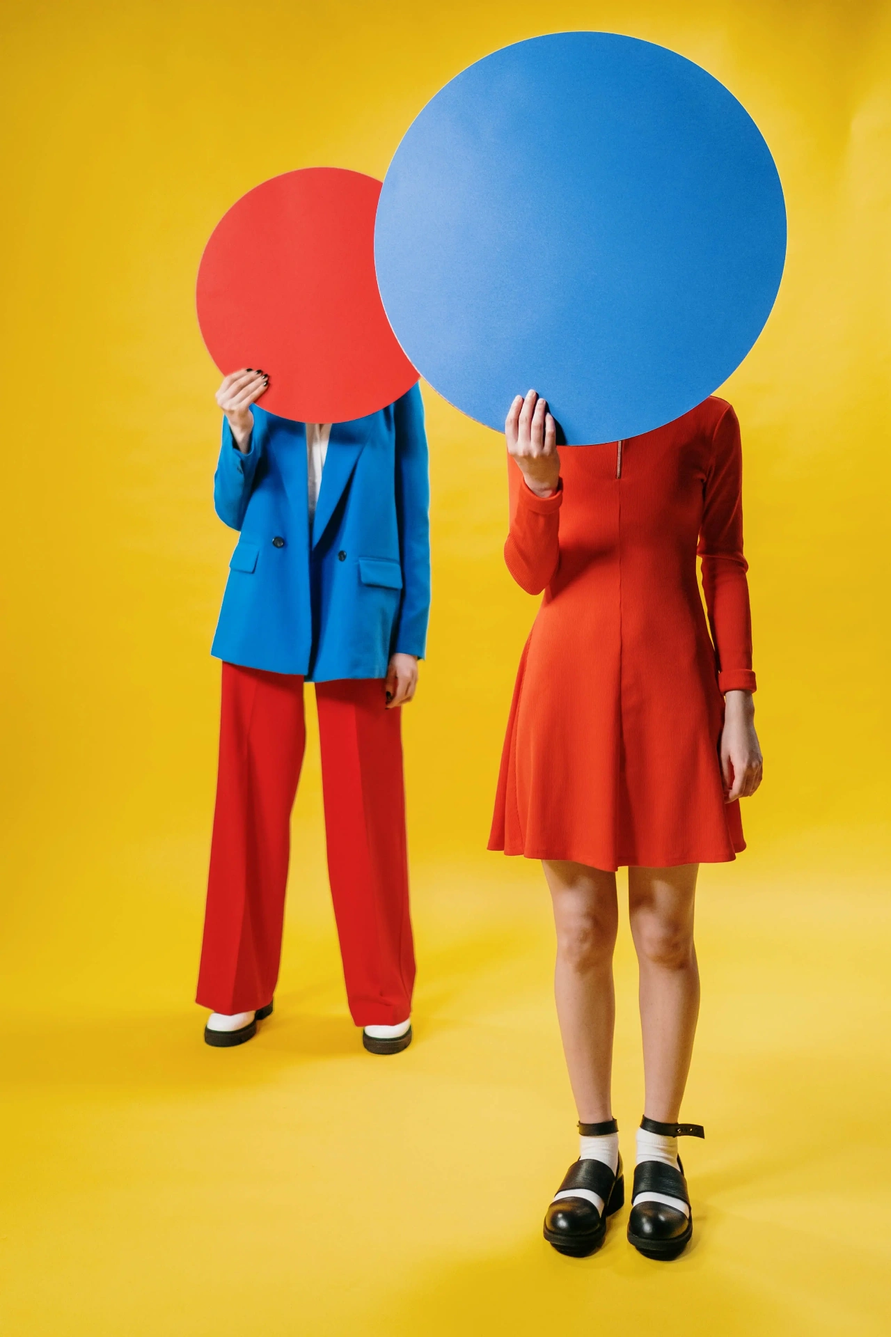 Two full-body models holding red and blue circular boards concealing their faces, by cottonbro studio.